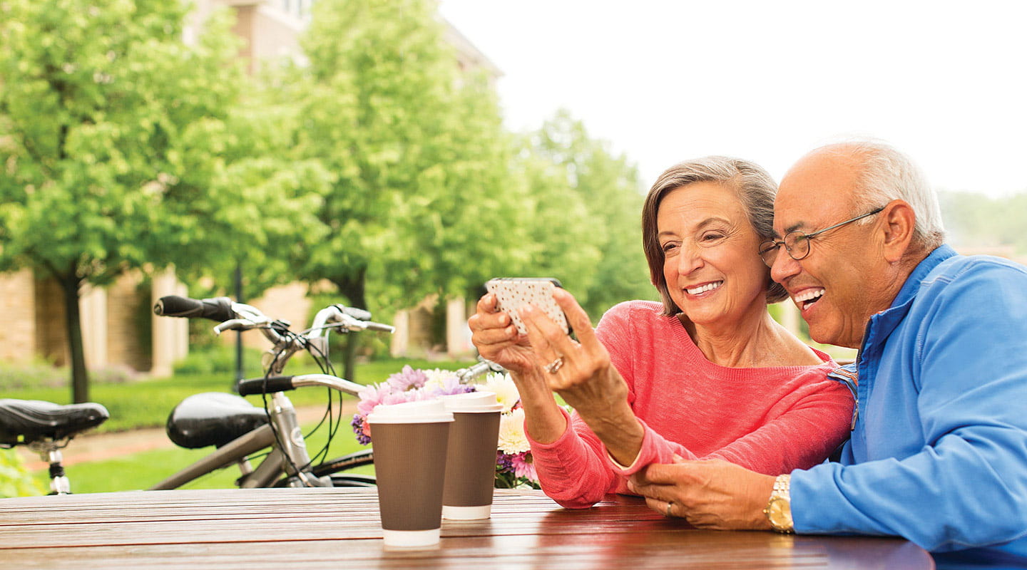A man and woman look into their phone and smile