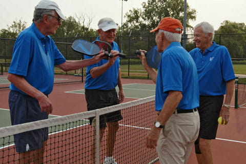 Four men tap paddles after a pickleball game.