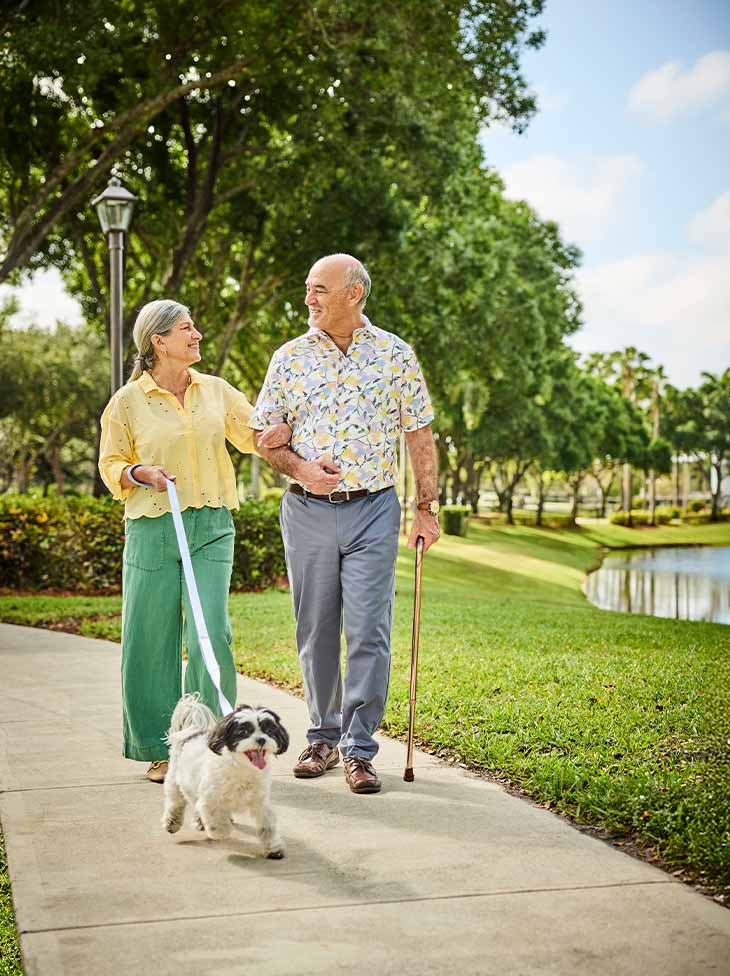 A man and a women walking a dog outside. 