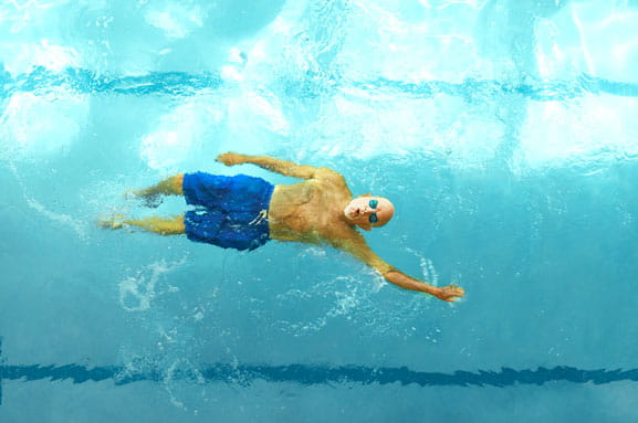 A man swims backstroke in a lap pool.