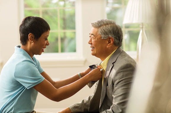 A care professional ties a bowtie for a man.