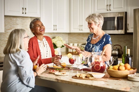 Three women stand and laugh in a kitchen.