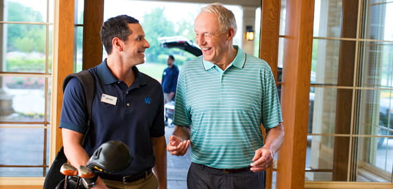 A Vi employee carries golf clubs while walking side by side with an older man.
