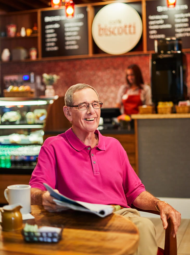 A man sits in front of a cafe in a senior living community.