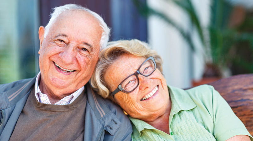 A man and woman smile, while the woman's head rests on his shoulder.