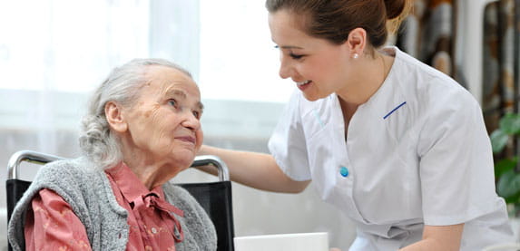 A care professional gives a bowl to an older woman.