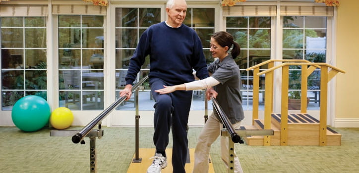 A care professional leads a man through physical therapy exercises.