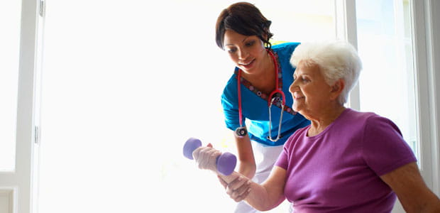 A nurse guides a woman with a weight in her hand.