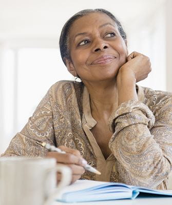 A woman looks into the distance while sitting with a pen and paper