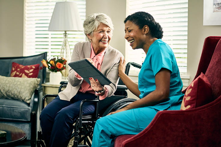 An older woman in a wheelchair and a woman in scrubs review something together.