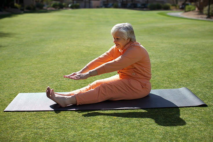 A woman on a yoga mat stretches her arms toward her toes.