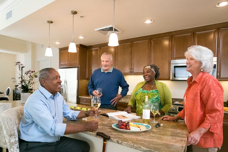 Two couples stand in a kitchen and drink wine.