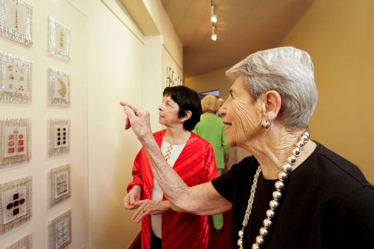 Two women look at artwork on a wall.