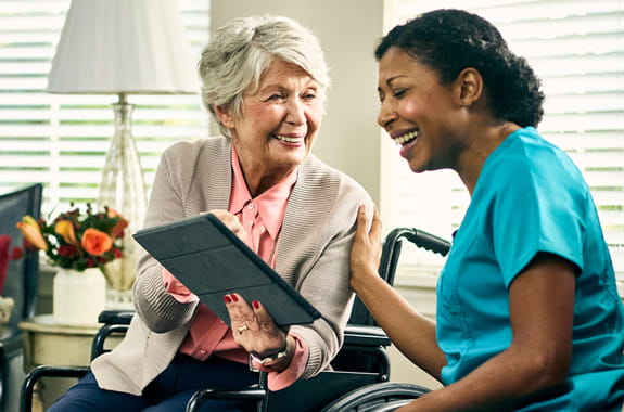 A woman in a wheelchair and a medical professional look at a tablet together.