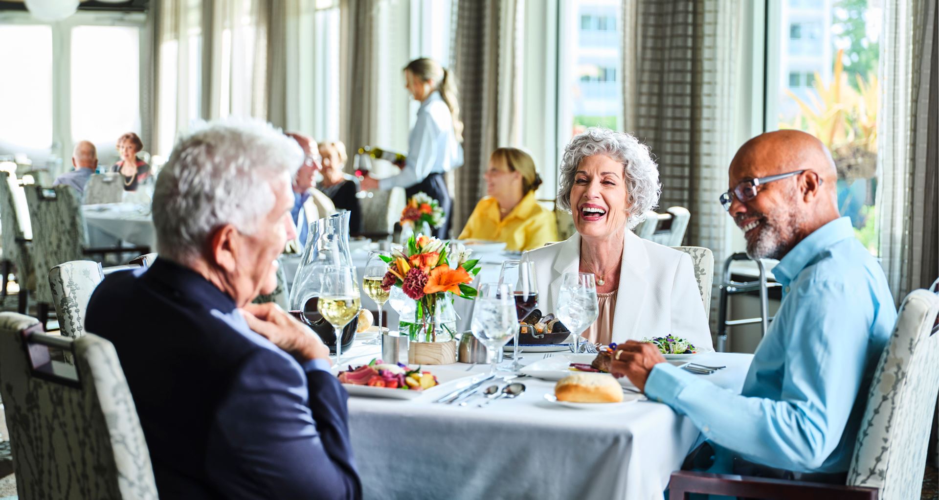 Friends laugh while enjoying a shared meal.