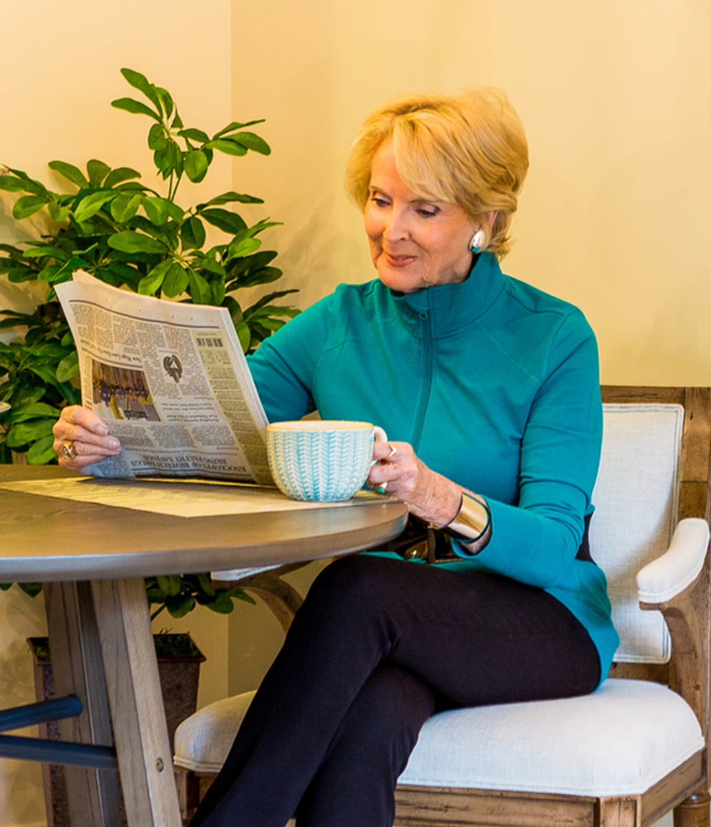 Woman sitting reading a news paper with mug in hand. 