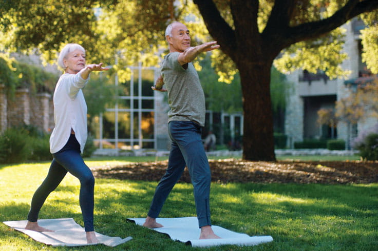 A couple does yoga outside.