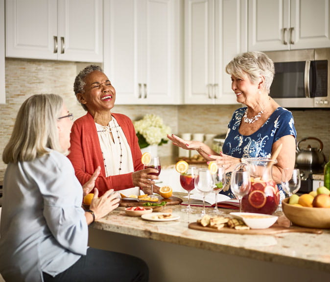 Women laugh in a kitchen while they drink sangria.