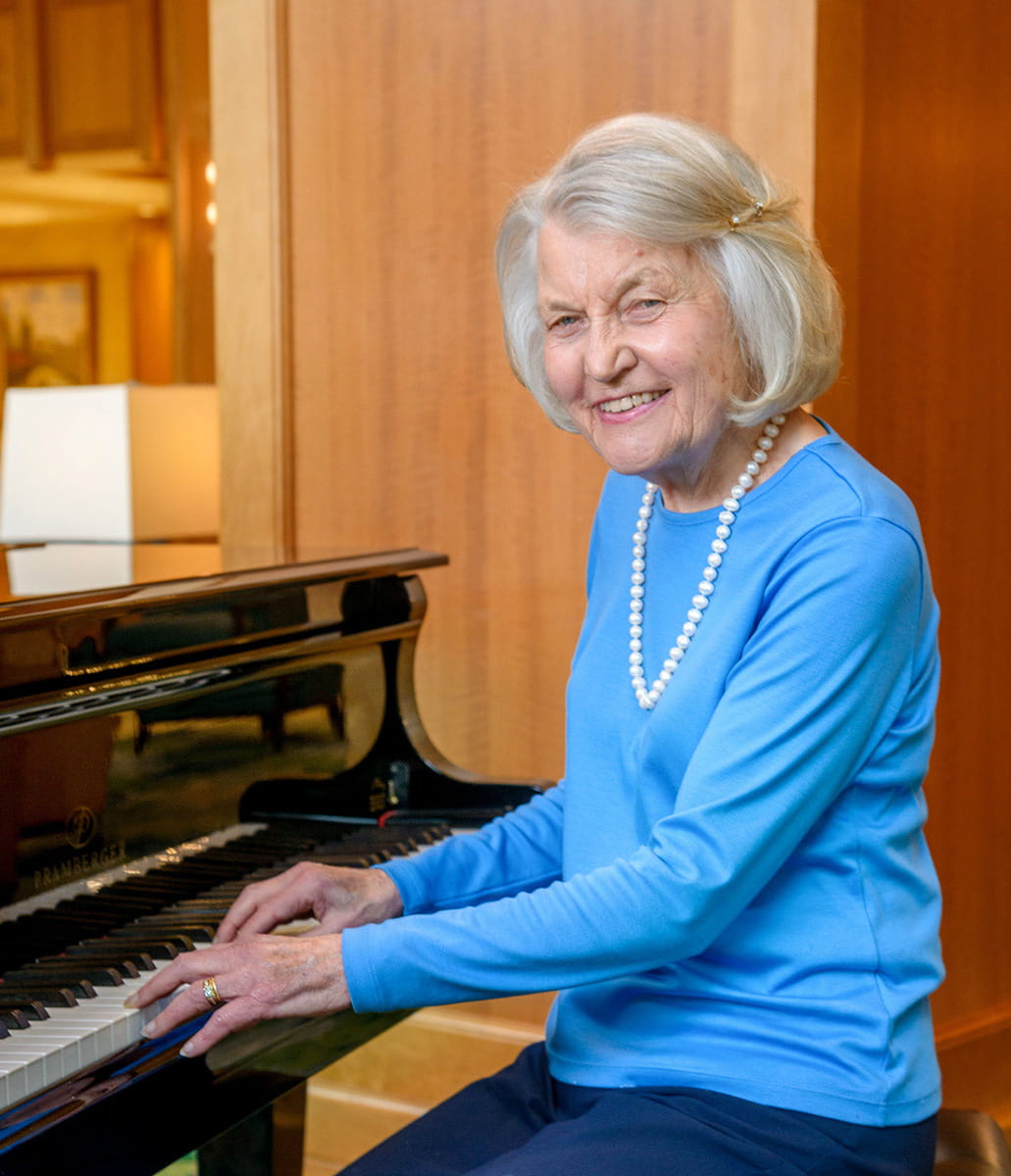 Woman in Vi at Palo Alto living playing the piano. 