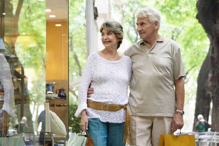 A man and woman walk down a street holding shopping bags.