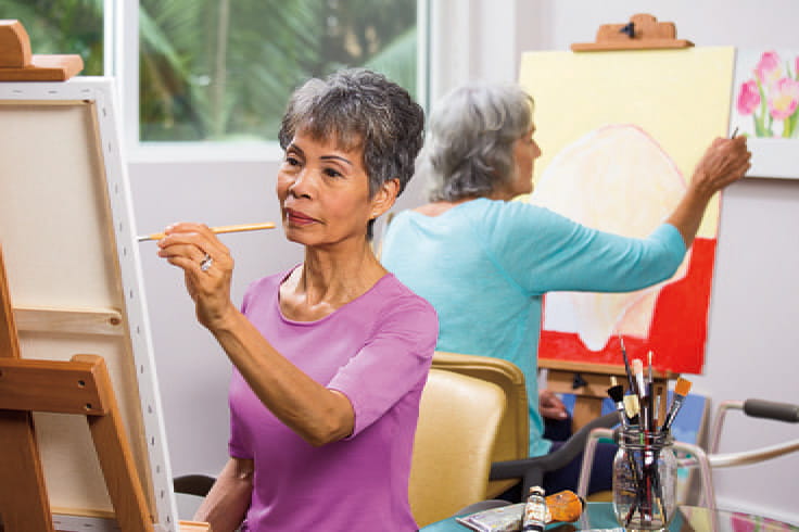 A woman in a purple shirt paints in the Vi at La Jolla Village art studio