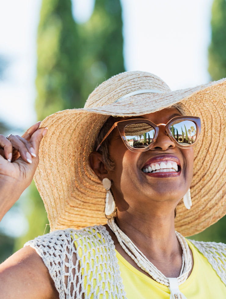 A woman wearing sunglasses and a hat smiles off camera.