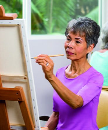 A woman in a purple shirt paints a canvas.