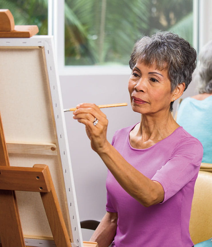 A woman in a purple shirt paints at an easel. 