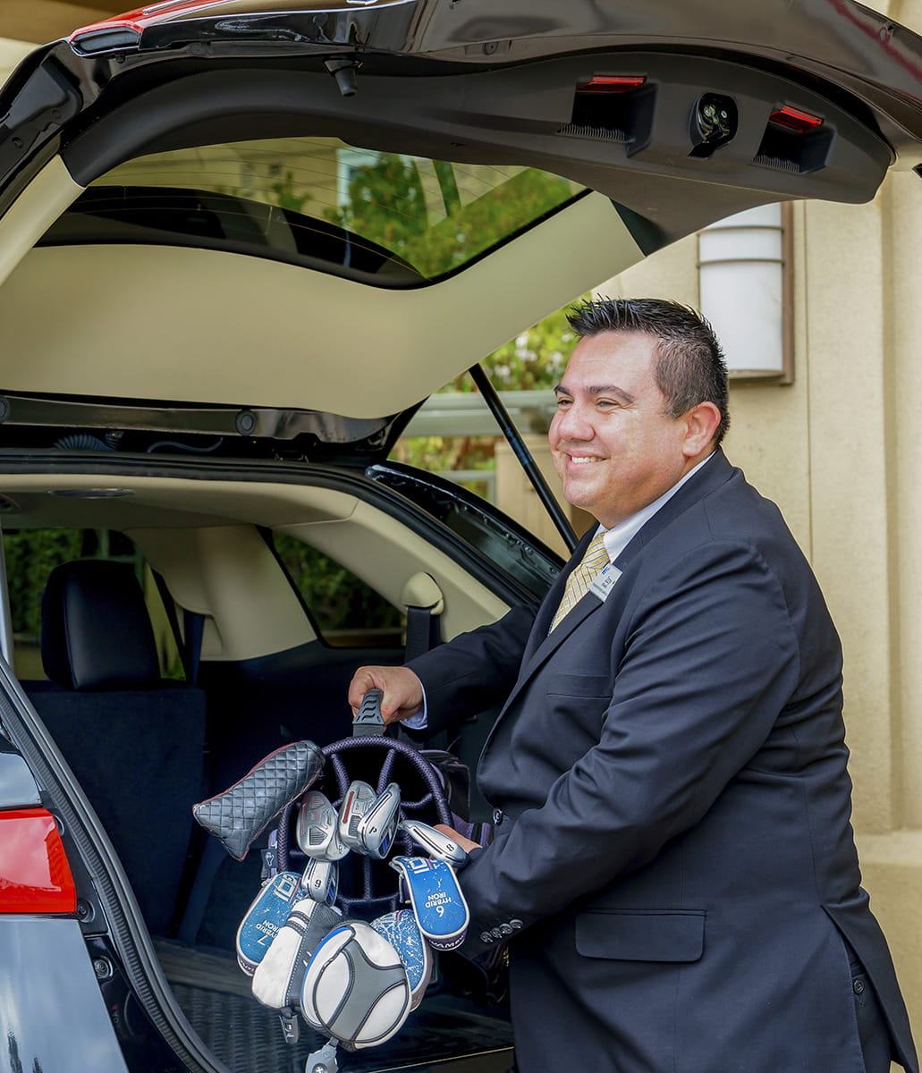 A valet unloads golf clubs from a car.