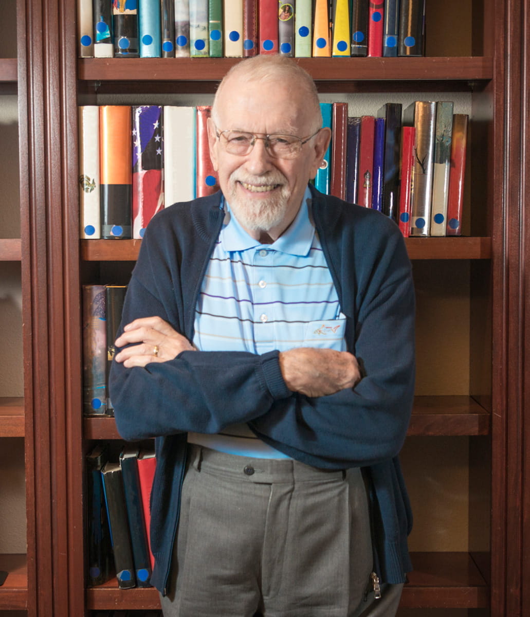 A man smiles while standing in front of a bookshelf.