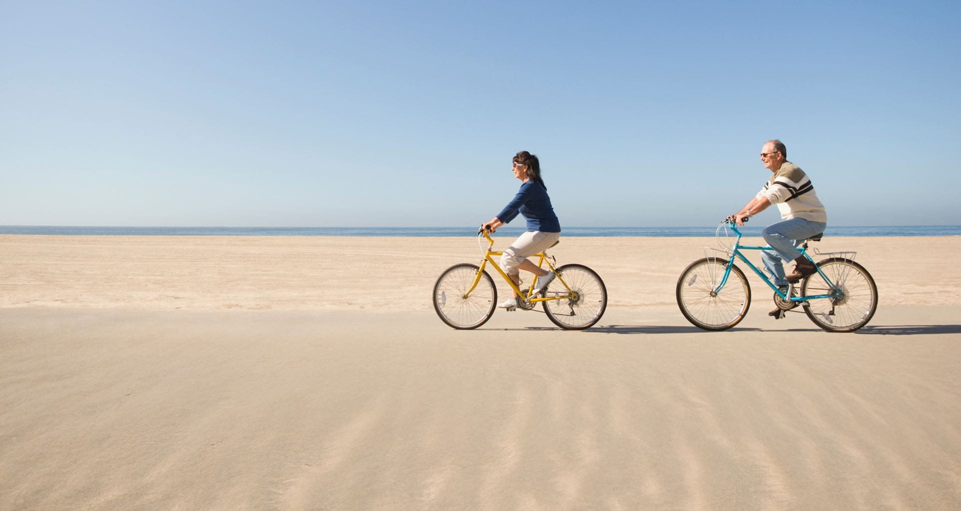 Two people ride bikes on the beach.