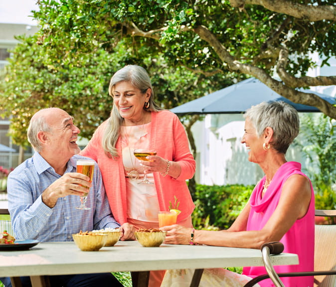 Two women and a man laugh together over cocktails outdoors.