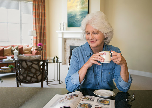A woman drinks from a mug at her dining room table.