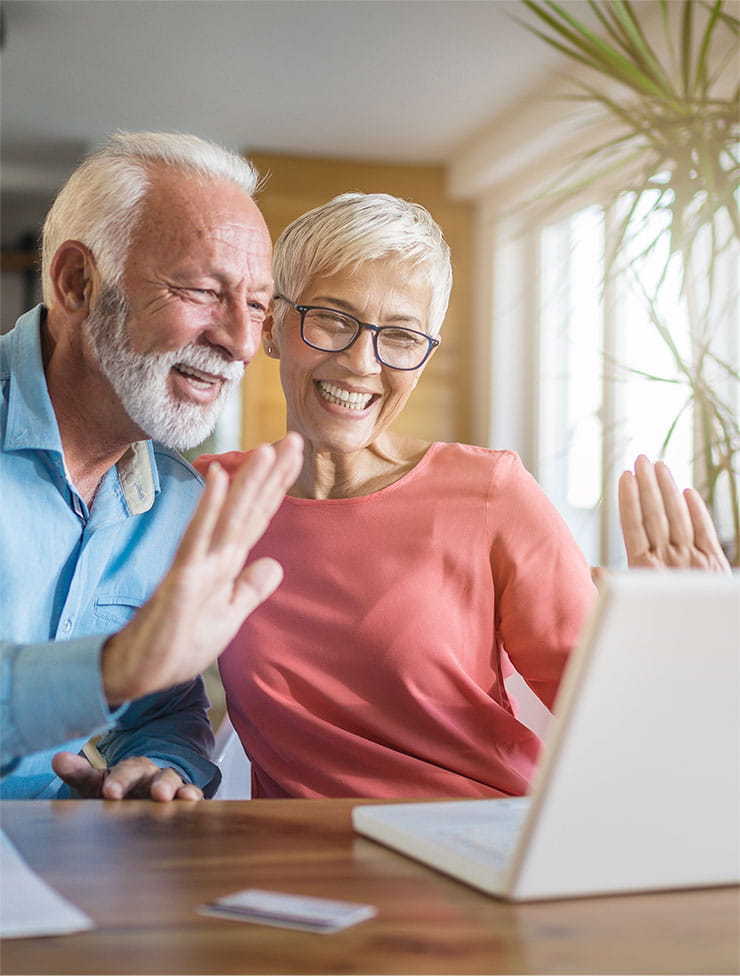 A couple smiles and waves at their laptop.