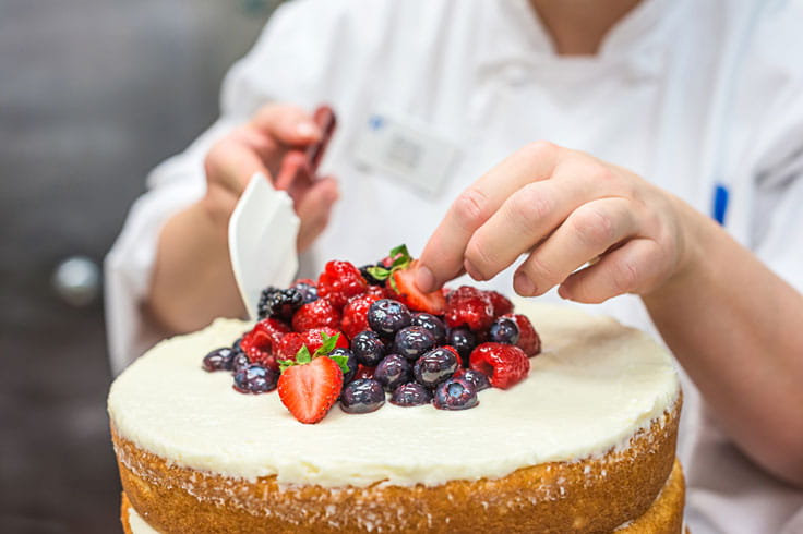 A pastry chef tops a cake with berries.