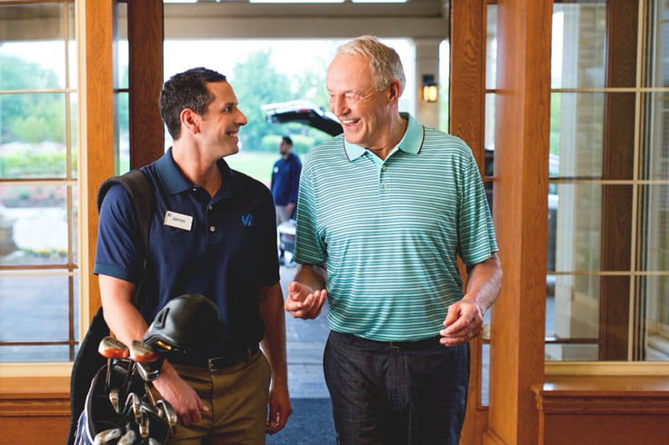A staff member holds a resident's golf clubs while they walk inside.