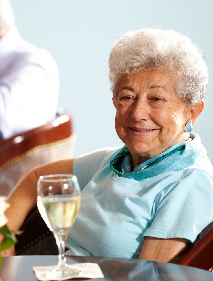 A woman in a blue top sits with a glass of white wine.