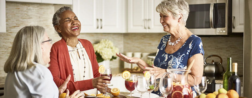 Three women laughing with drinks in a kitchen