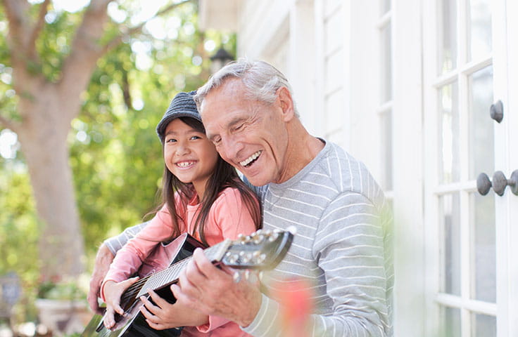 An older gray-haired man plays guitar with a young girl