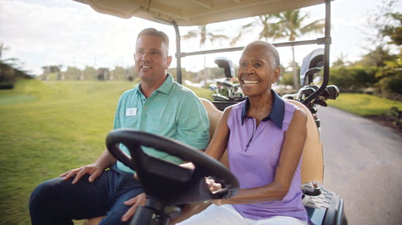 A resident drives a golf cart while sitting next to a man.