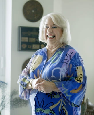 Resident Carol Ures stands smiling in her living room.