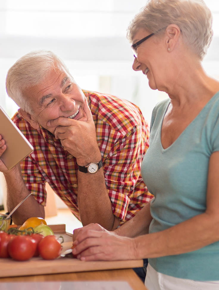 A couple laughing in the kitchen while preparing food