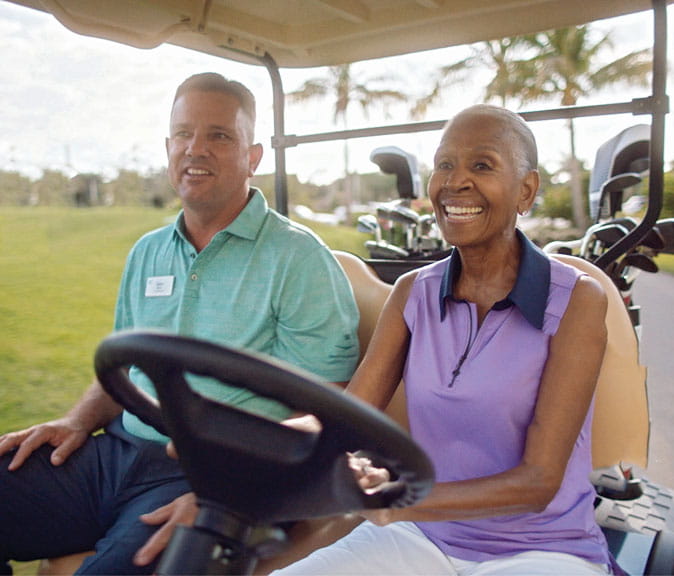 A woman drives a golf cart alongside the community's golf pro.