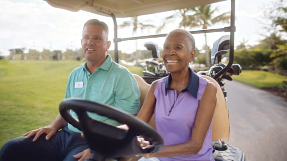 A woman drives a golf cart with Stan Geer, the on-site golf pro.