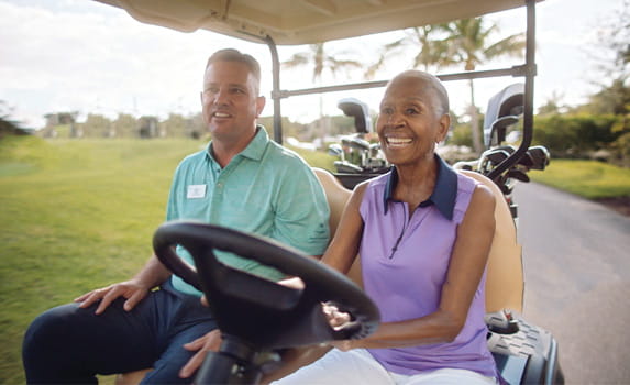 Vi at Bentley Village's golf pro rides in a golf cart with a smiling woman.