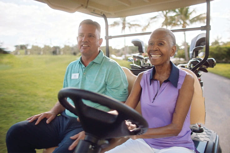 A golf pro and resident ride in a golf cart.