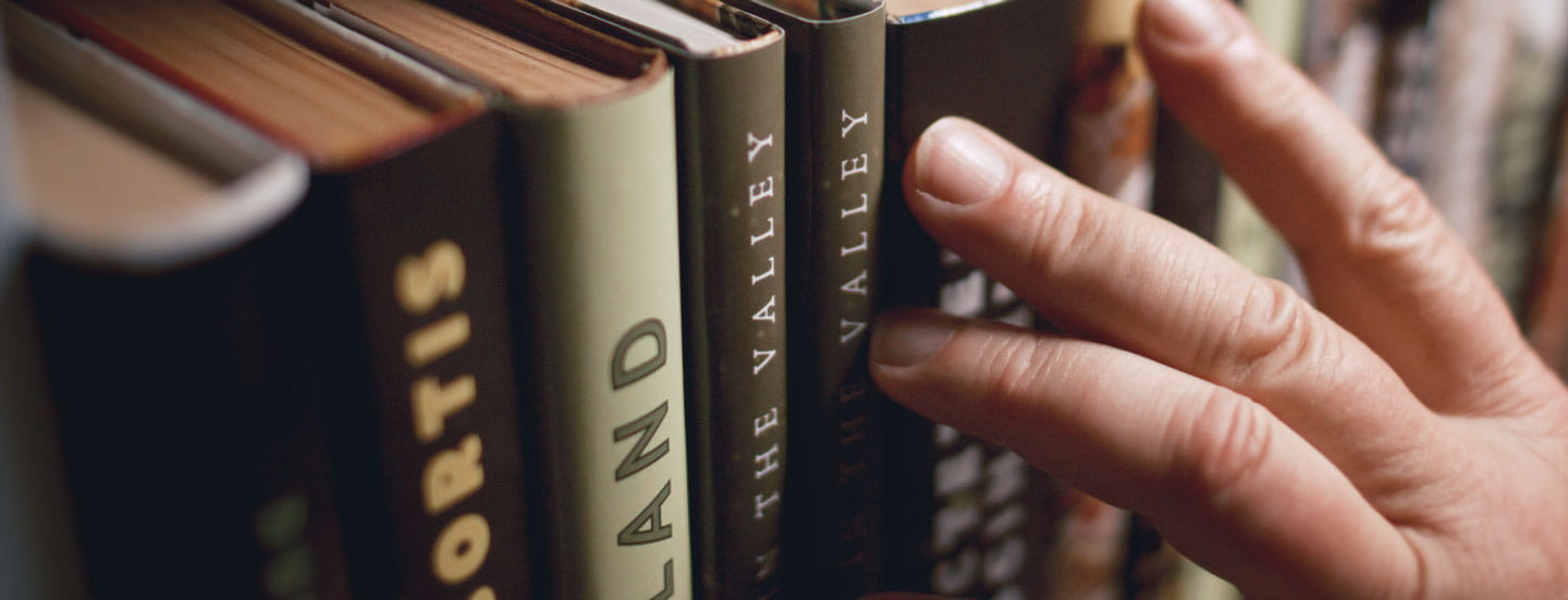 A close-up shot of fingers skimming books in a library.