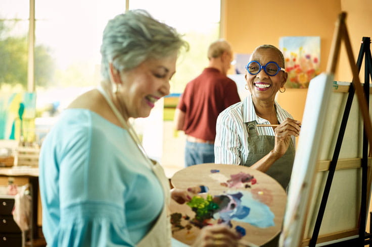 Two women smile in a painting class.