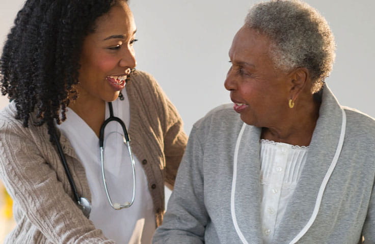 A healthcare worker helps guide a woman using a walker.