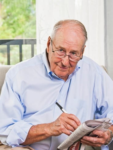 A man holding a newspaper and pen smiles at the camera.